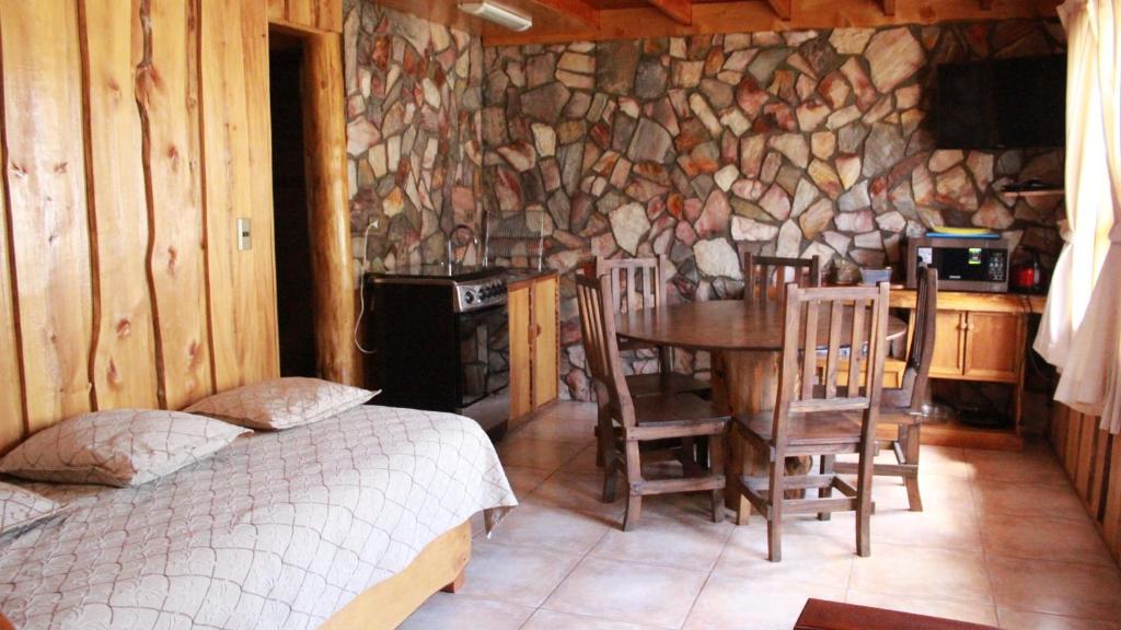 1 dormitorio con mesa, sillas y pared de piedra en Cabañas Aitue, en Futaleufú