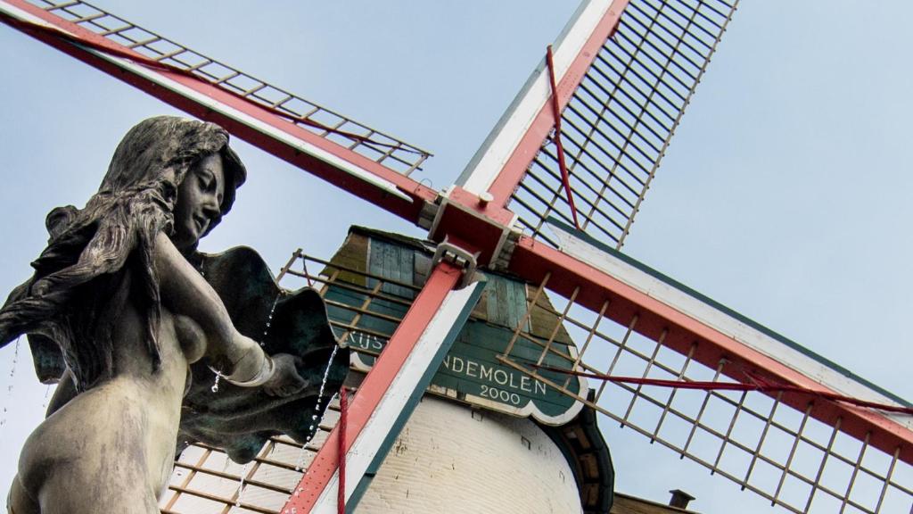 een standbeeld van een vrouw die naast een windmolen staat bij Rysselende Molen in Ardooie