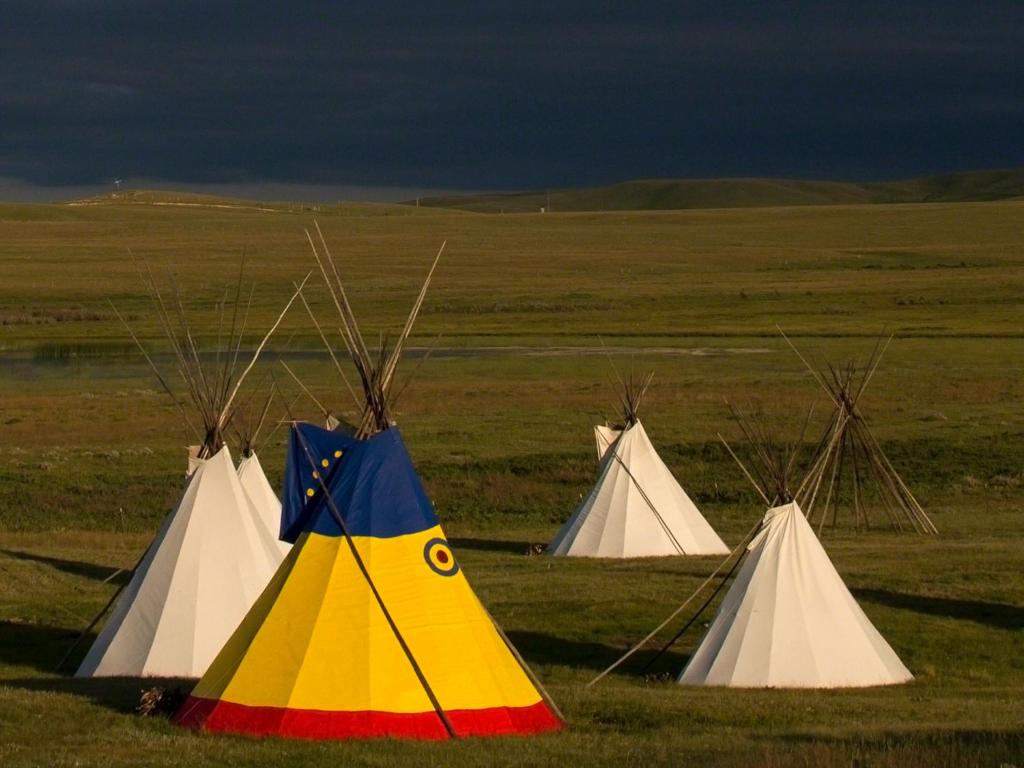 a group of tents in a field with a storm at Lodgepole Gallery in Browning