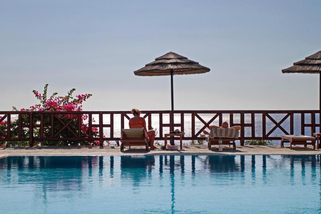 a person sitting in chairs next to a swimming pool at Aegean Village Beachfront Resort in Amoopi
