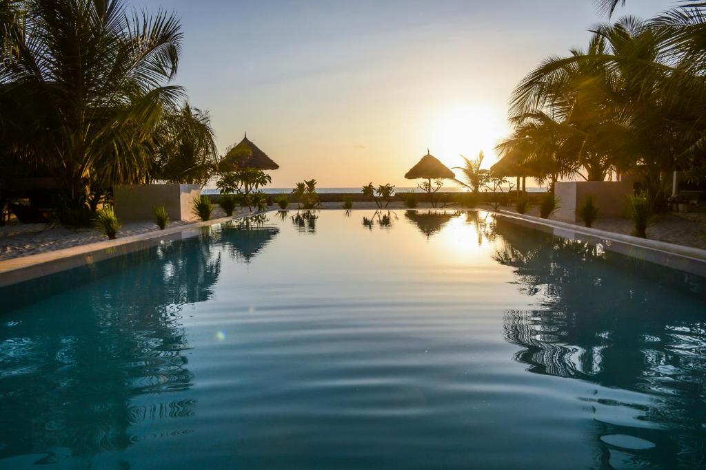 a swimming pool with the sun setting in the background at Nur Beach Hotel in Jambiani