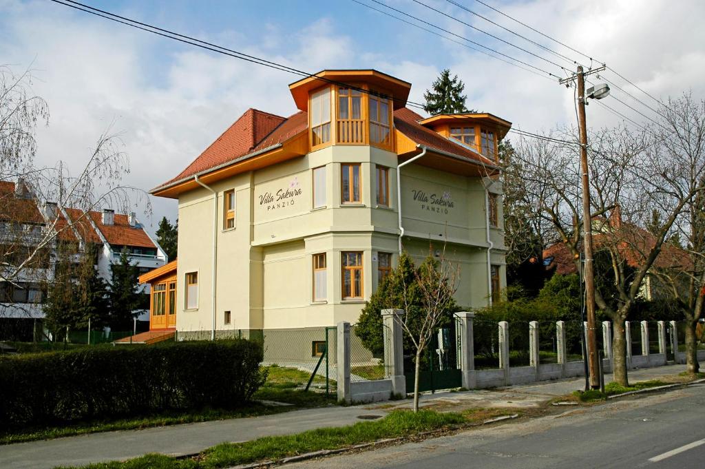 a large house with a red roof on a street at Villa Sakura Panzió in Sopron