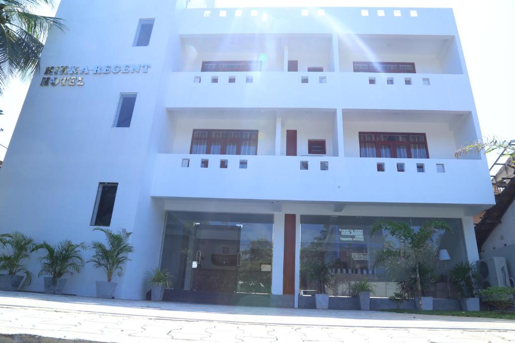 a white building with palm trees in front of it at Hikka Regent Hotel in Hikkaduwa