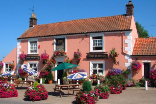 a pink building with benches and umbrellas in front of it at Rosebud cottage in Corton