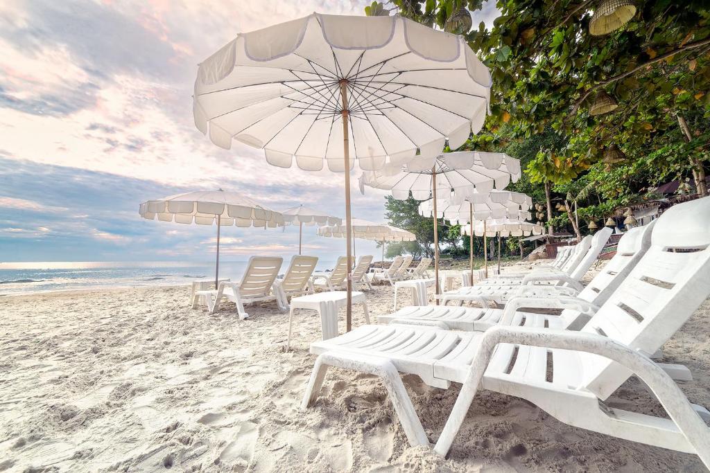 un grupo de sillas y sombrillas blancas en una playa en Samed Villa Resort, en Ko Samed