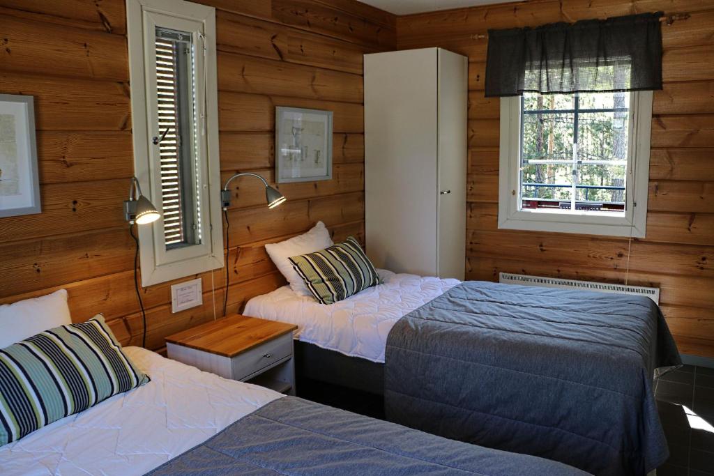 two beds in a room with wooden walls and windows at Rauhalahti Holiday Homes in Kuopio