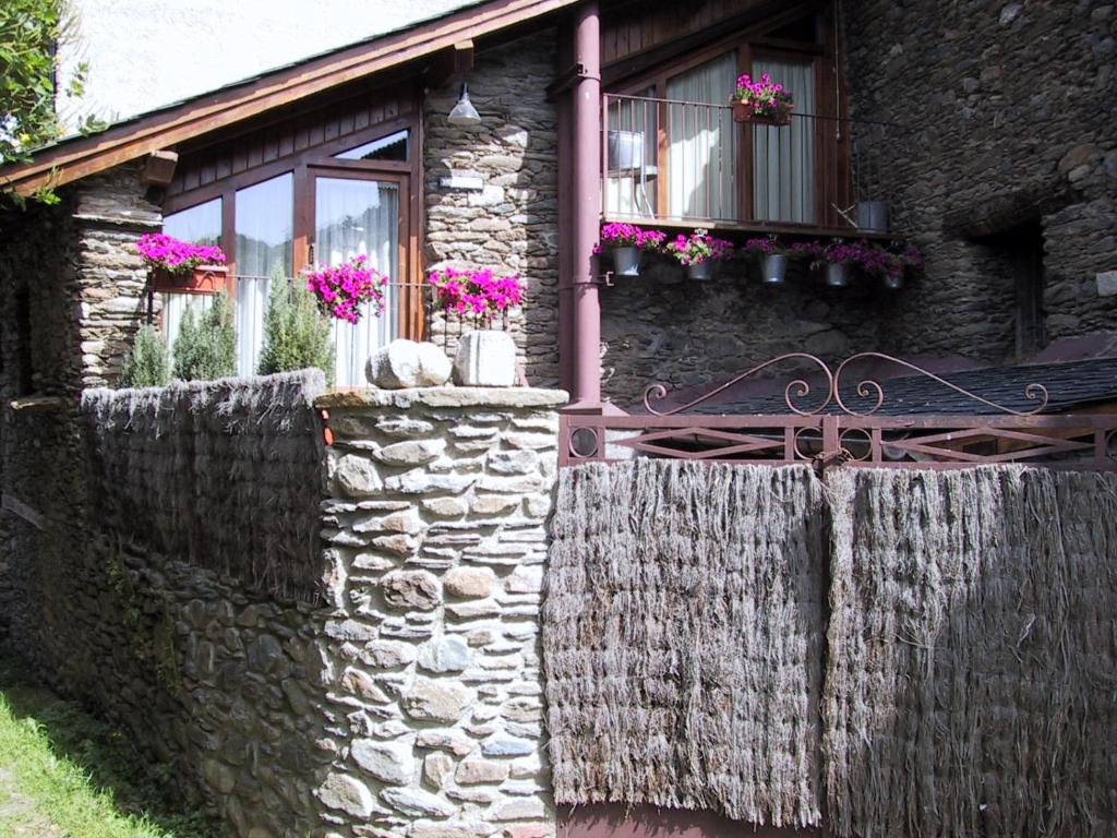a stone house with a stone fence and flowers at La Llúpia in Isavarre
