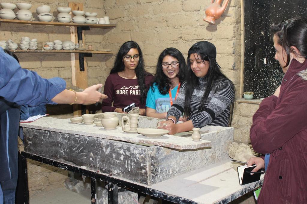 um grupo de mulheres em pé em torno de uma mesa fazendo cerâmica em Posada El Artesano De Raquira em Ráquira