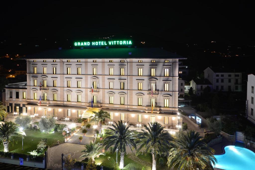 a large white building with palm trees in front of it at Grand Hotel Vittoria in Montecatini Terme