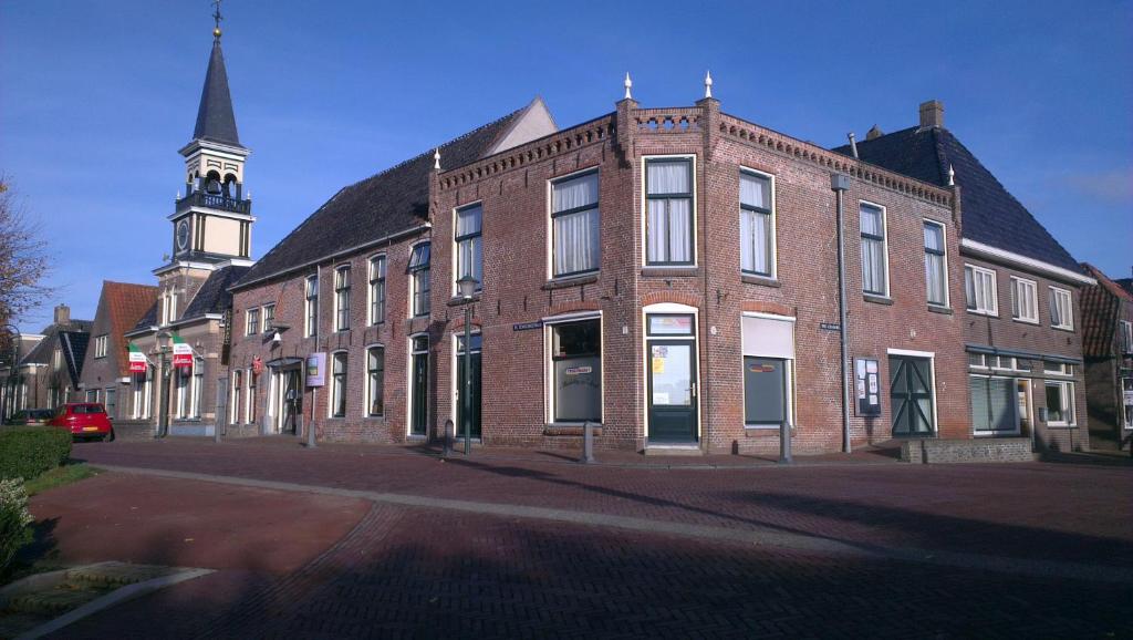 un gran edificio de ladrillo con una torre de reloj en una calle en Logement 'De witte klok' en Oude Bildtzijl