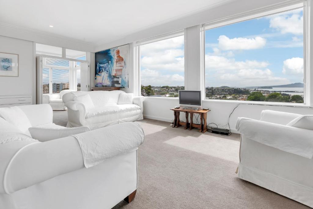 a living room with white furniture and large windows at Spacious Sunny Seaview Apartment in Auckland