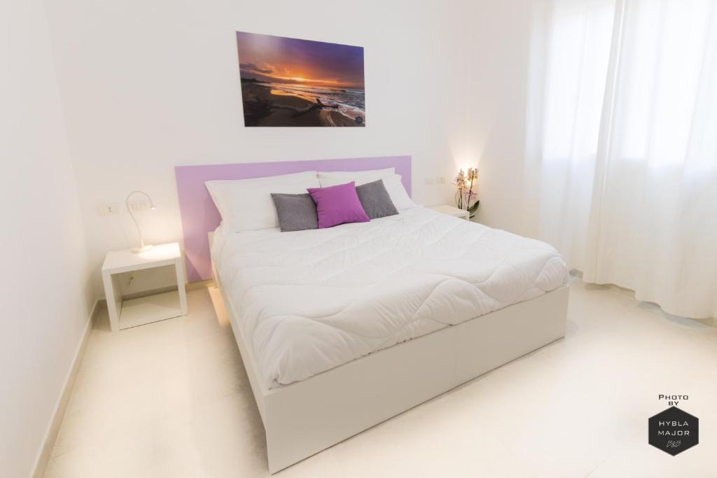 a white bedroom with a large white bed with purple pillows at Hybla Major B&B in Avola