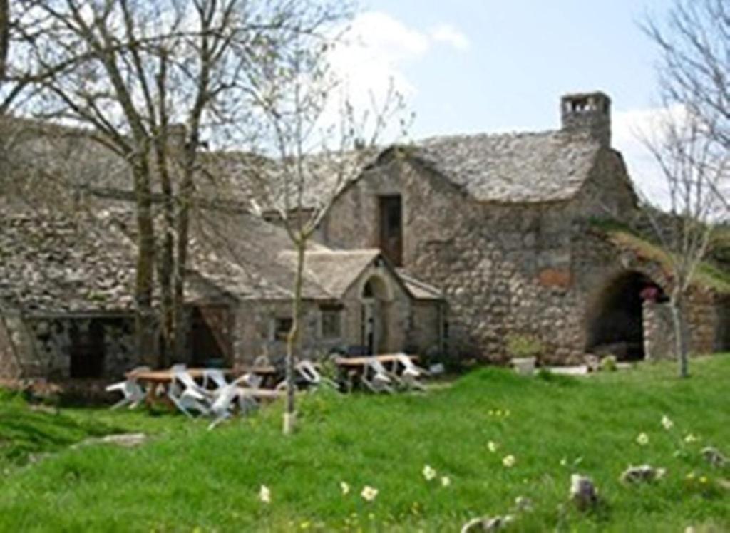 un edificio de piedra con mesas de picnic delante de él en Ferme Auberge La Tindelle, en La Cresse