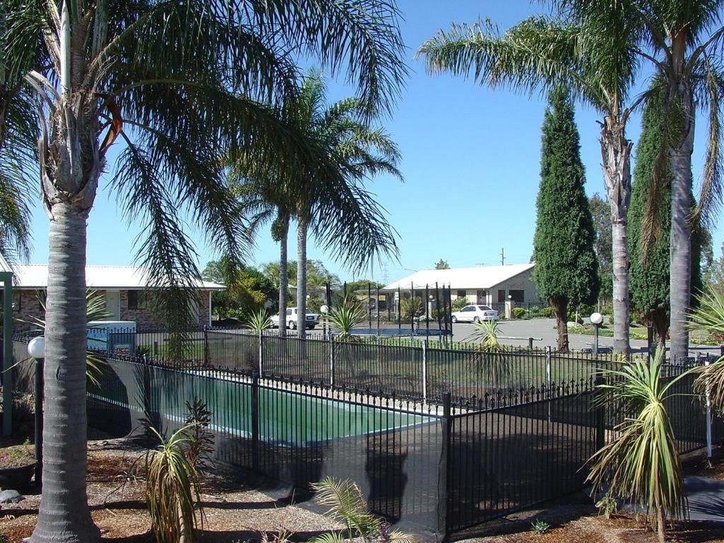 a swimming pool with palm trees and a fence at Palm Valley Motel in Tarro