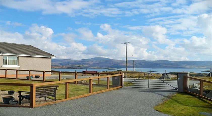 a house with a fence and a bench in front of the water at Riverside in Tarbert