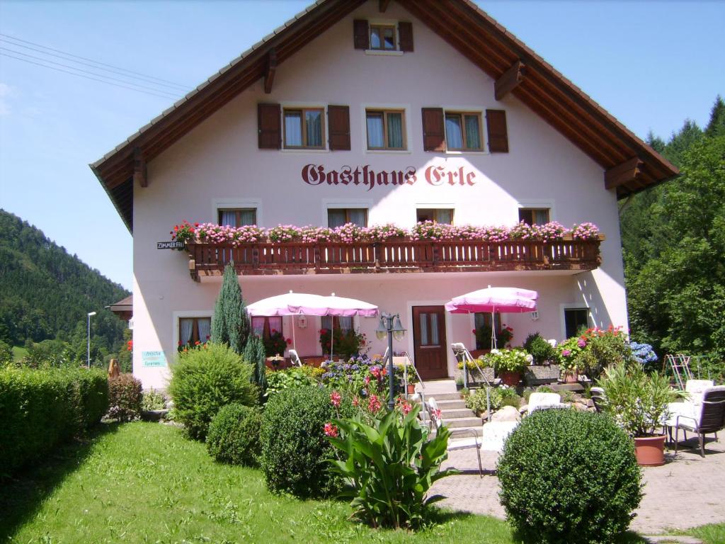 a large white building with a balcony with pink umbrellas at Gasthaus Zur Erle in Simonswald