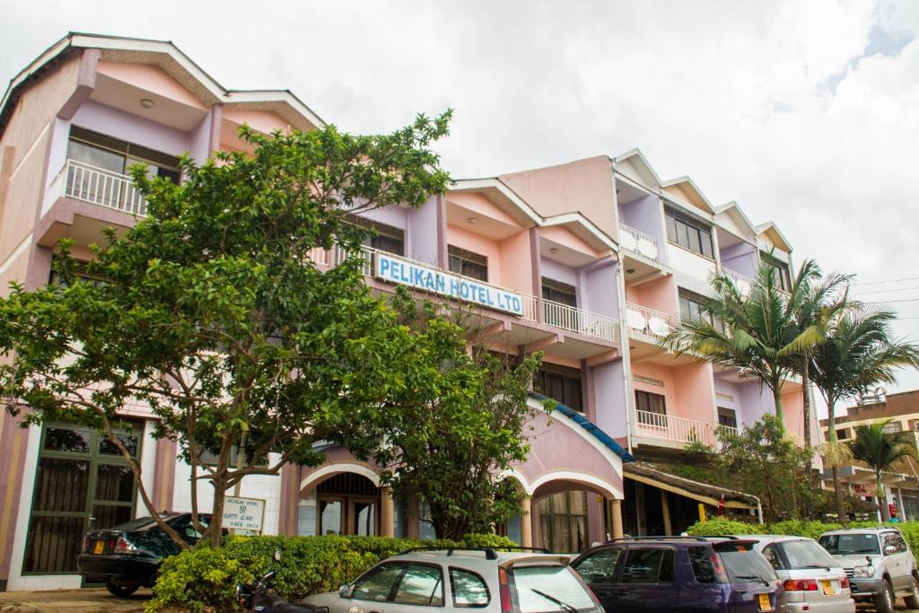 un bâtiment rose avec des voitures garées devant lui dans l'établissement Pelikan Hotel, à Mbarara