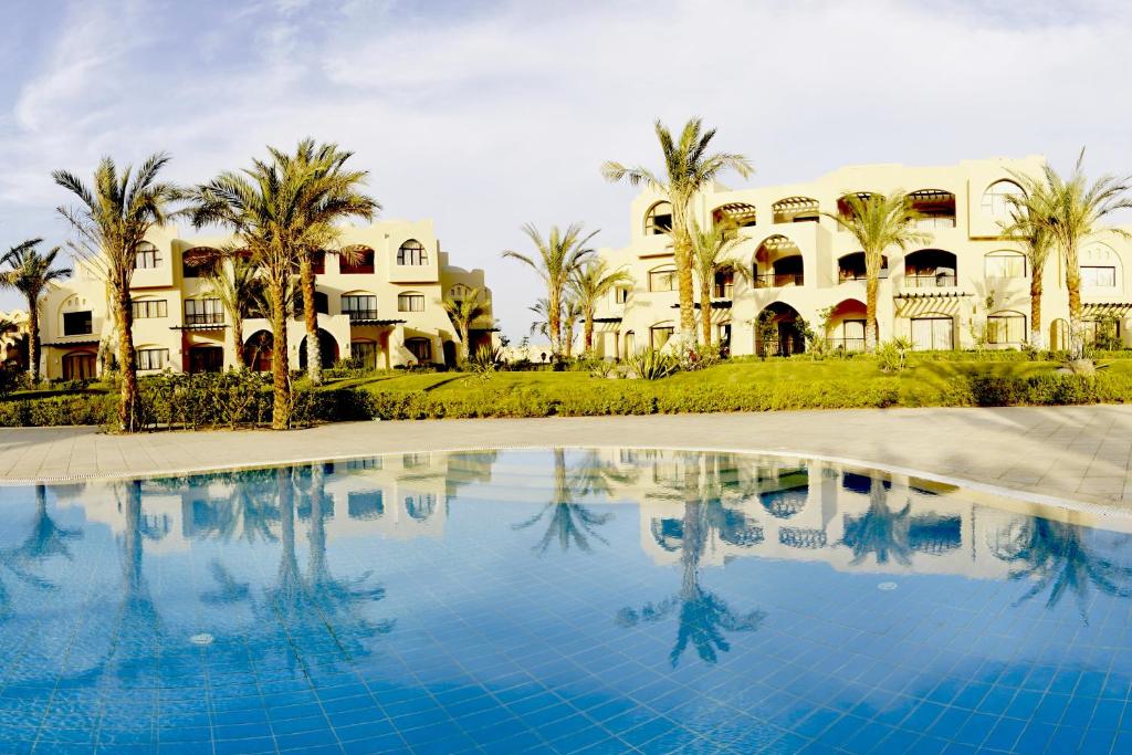 un bâtiment avec des palmiers et une piscine dans l'établissement Jaz Makadi Saraya Palms, à Hurghada
