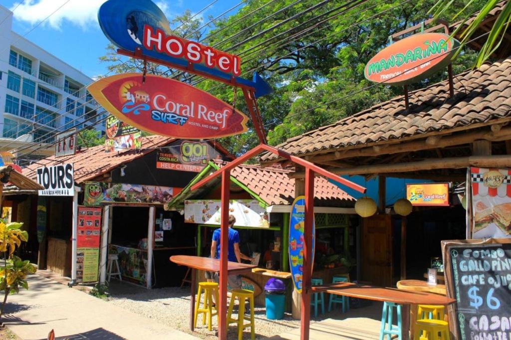 a hostel with tables and signs in front of it at Coral Reef Surf Hostel and Camp in Tamarindo