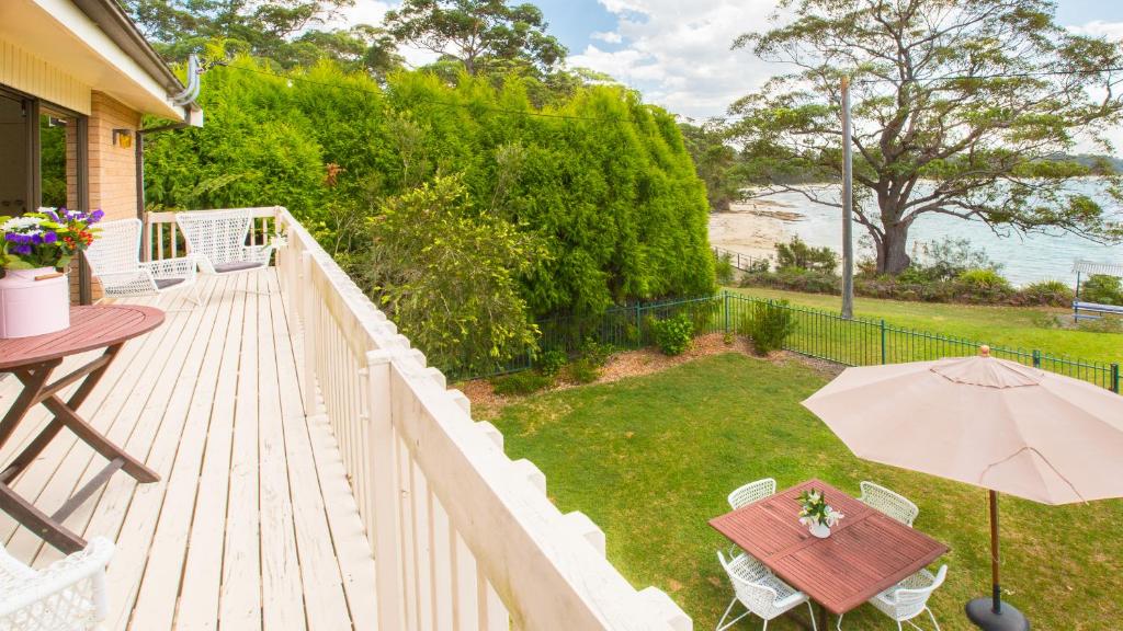 una terraza de madera con mesa y sombrilla en Driftwood Beachfront @ Vincentia, en Vincentia