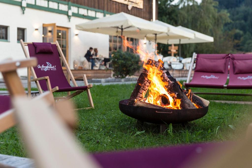 eine Feuerstelle im Gras mit Stühlen und einem Regenschirm in der Unterkunft Hotel Hörterer Der Hammerwirt in Siegsdorf