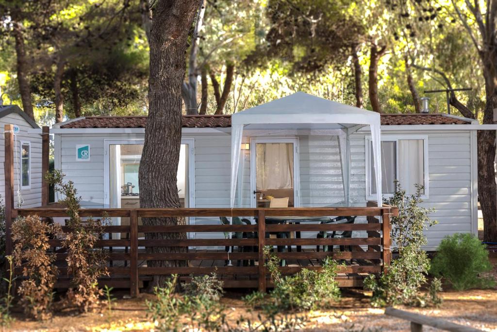 a white cabin with a tree and a fence at Giannella Camping in Orbetello