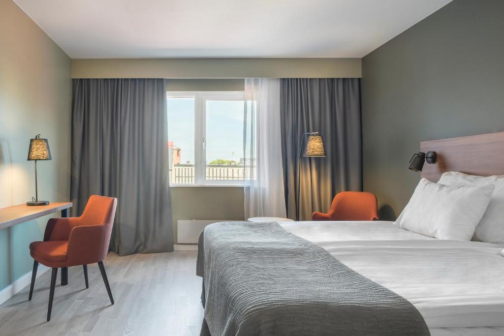 a hotel room with a bed and two chairs and a window at Quality Hotel Grand Kristianstad in Kristianstad