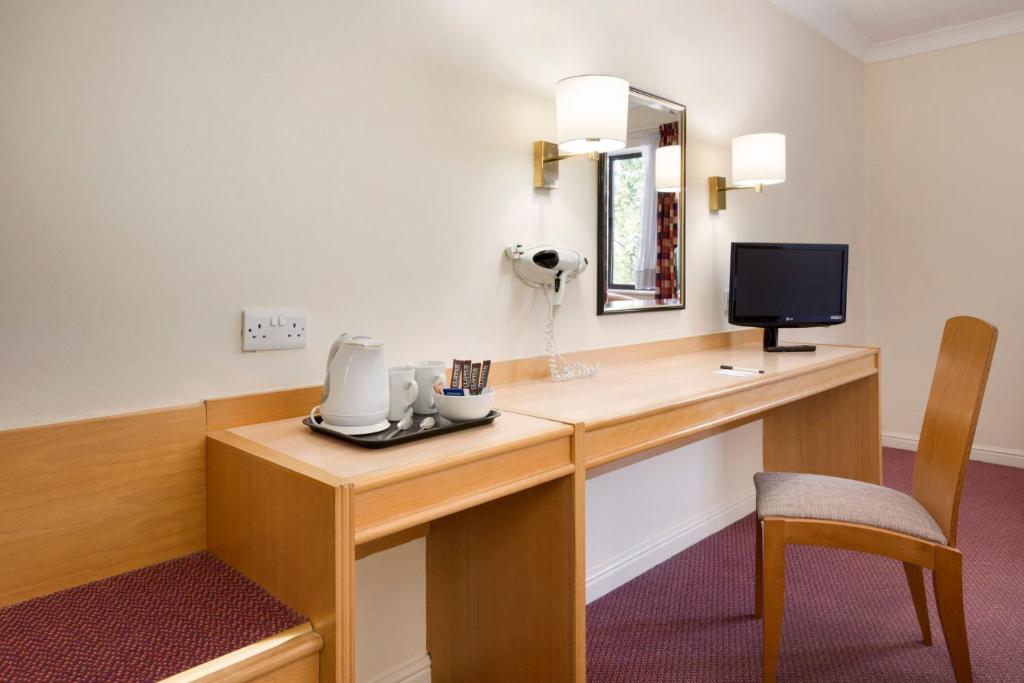 a room with a desk with a phone and a television at Days Inn Tewkesbury in Strensham