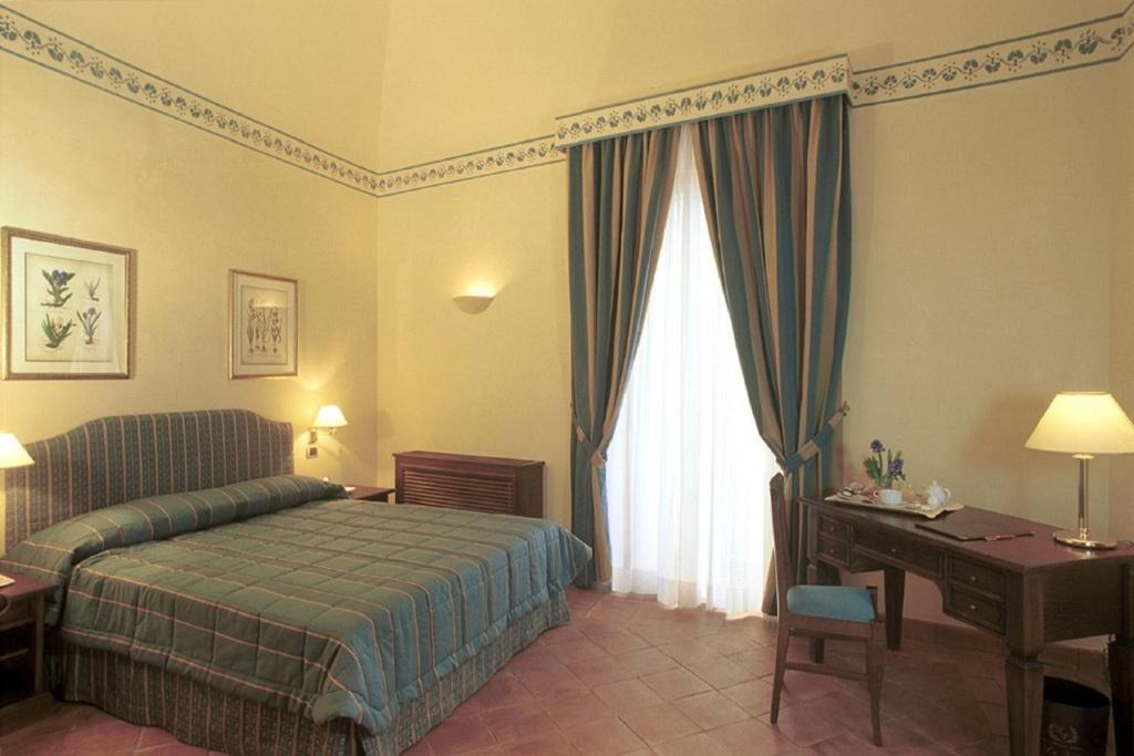 a bedroom with a bed and a desk and a window at Hotel La Ville in Catania