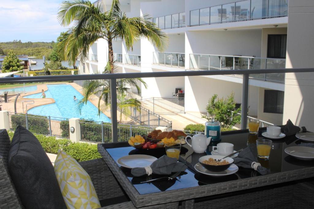 einen Tisch mit Speisen auf einem Balkon mit Poolblick in der Unterkunft The Boathouse Luxury Apartments in Tea Gardens