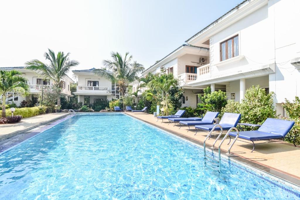 una piscina con sillas azules y un edificio en Rainforest - Casa Azure 5 Min walk to the beach en Calangute