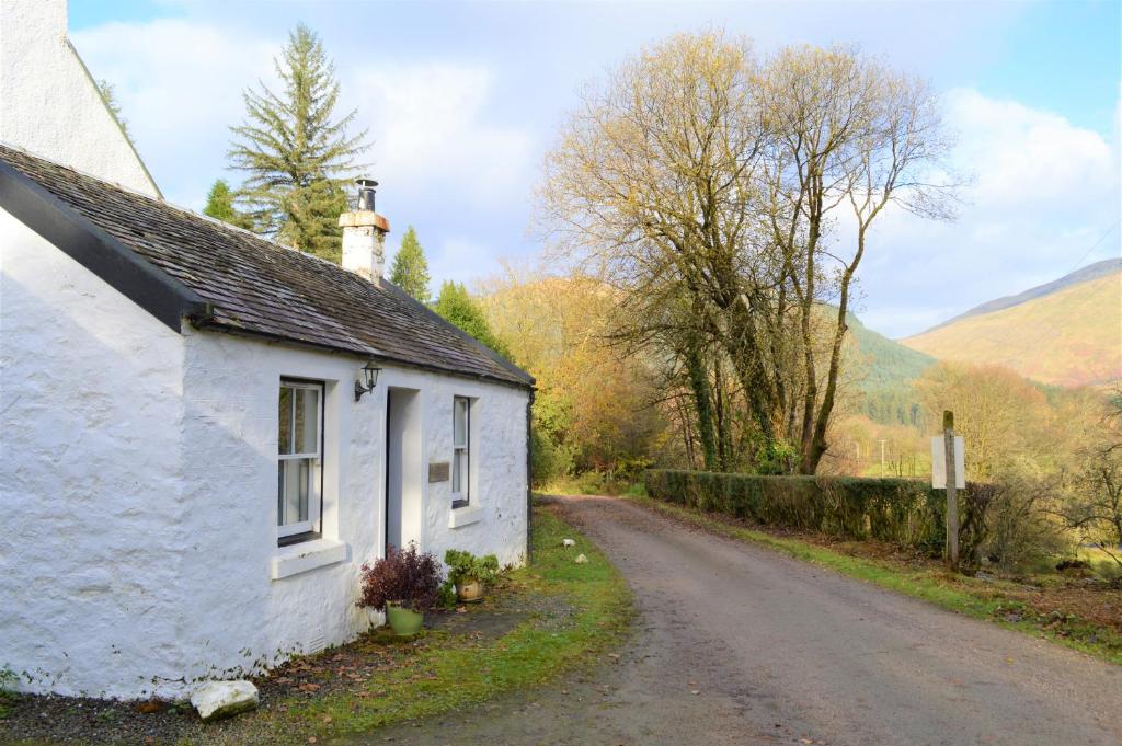 a small white cottage on a dirt road at Glenbranter Cottage in Strachur