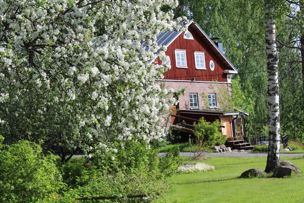 une maison avec un toit rouge et un arbre avec des fleurs blanches dans l'établissement Nukula Guestrooms, à Oravasaari