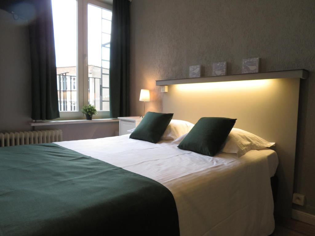 a bedroom with a large white bed with two green pillows at Hotel Notre Dame in Bruges