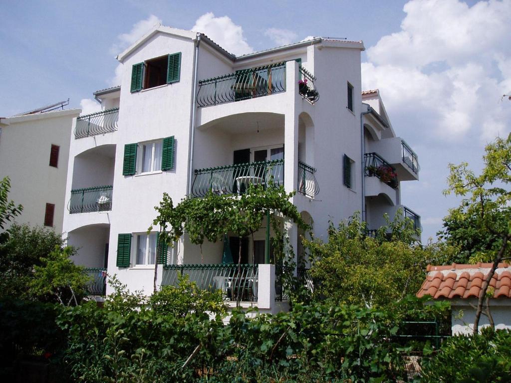 biały apartamentowiec z balkonami i drzewami w obiekcie Apartments Nada w mieście Vodice