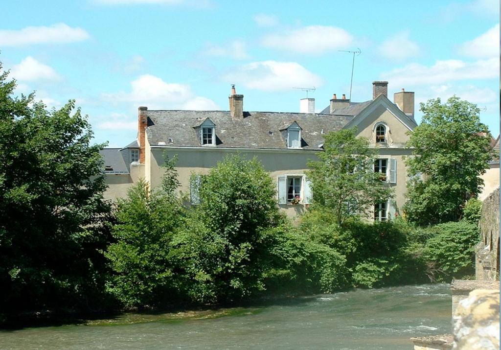 a large house with trees in front of a river at Chambres d'hôtes Le Pont Romain in Montfort-le-Gesnois