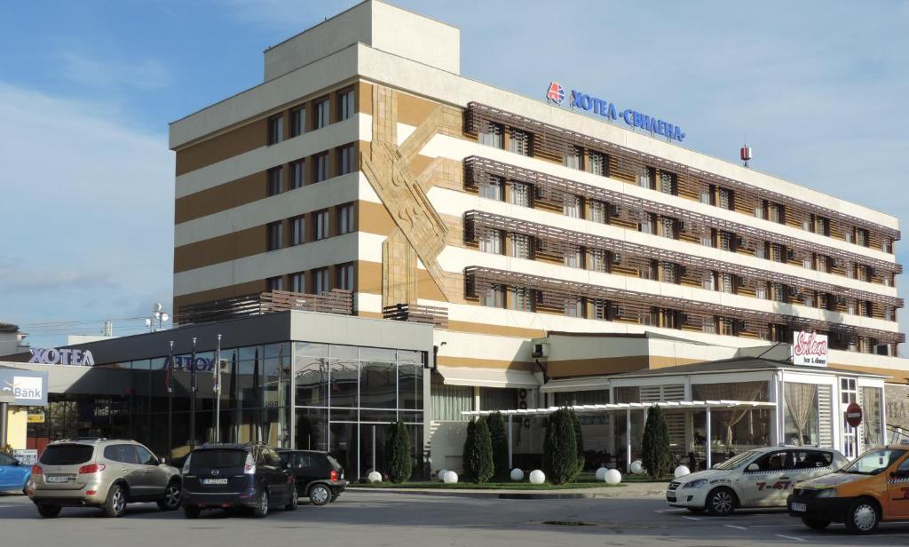 een groot gebouw met auto's geparkeerd op een parkeerplaats bij Hotel Svilena in Svilengrad