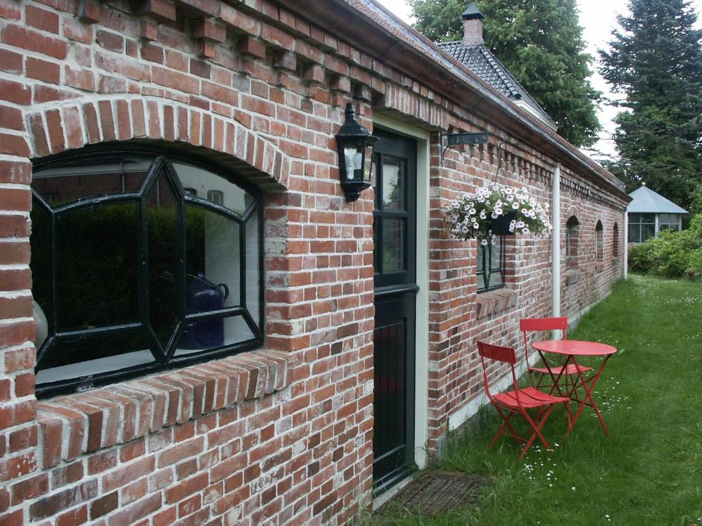 a brick house with two red chairs and a table at De Wilgenhof in Finsterwolde