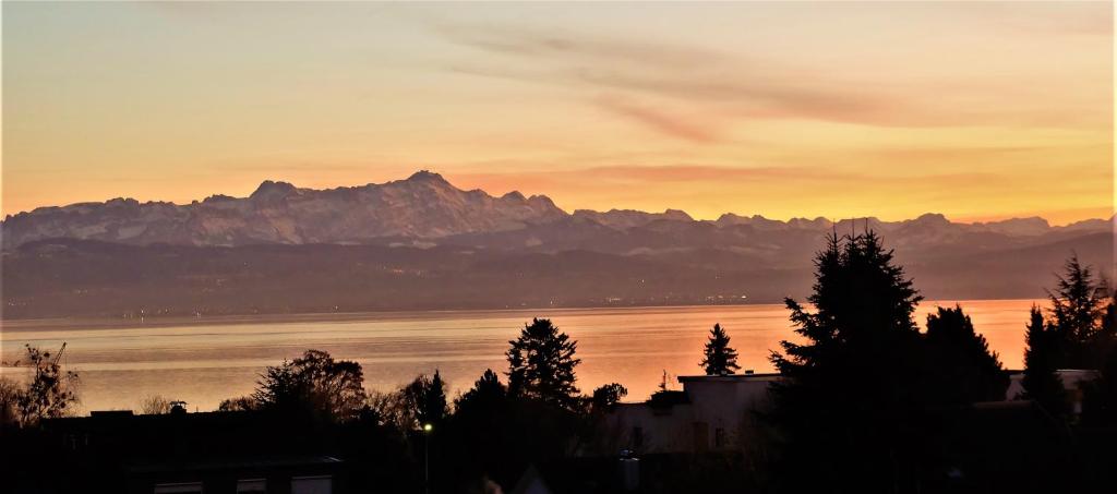 フリードリヒスハーフェンにあるBodenSEE Apartment Friedrichshafen "DACHTERRASSE"の山を背景に水上夕日