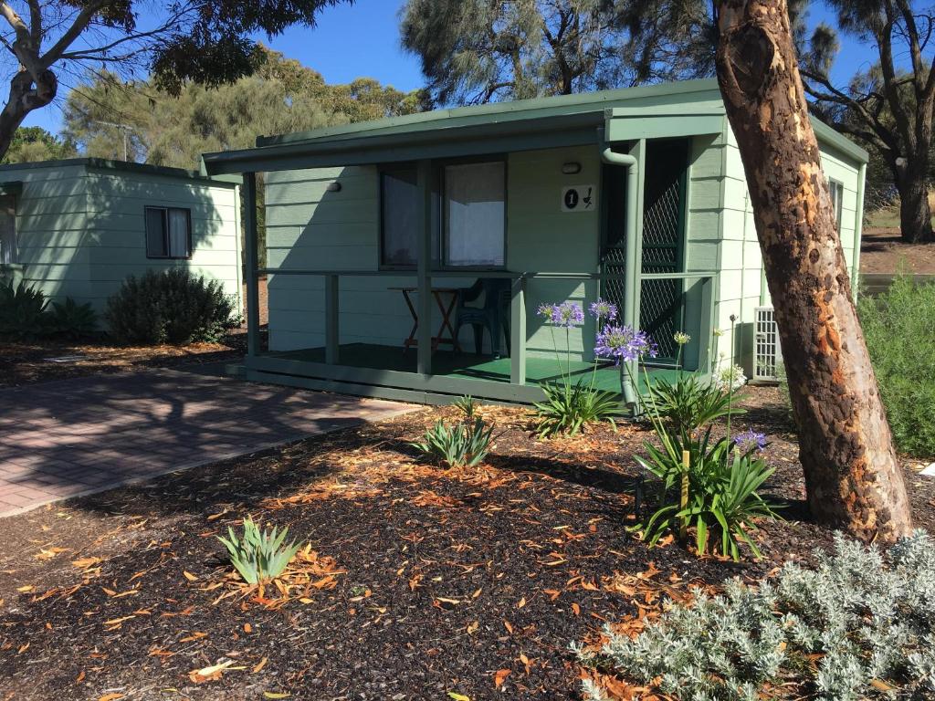 a green cottage with a tree and flowers at Lake Albert Caravan Park in Meningie