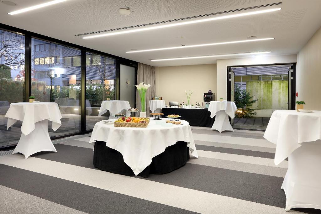 a restaurant with white tables and chairs and windows at Eurostars Book Hotel in Munich