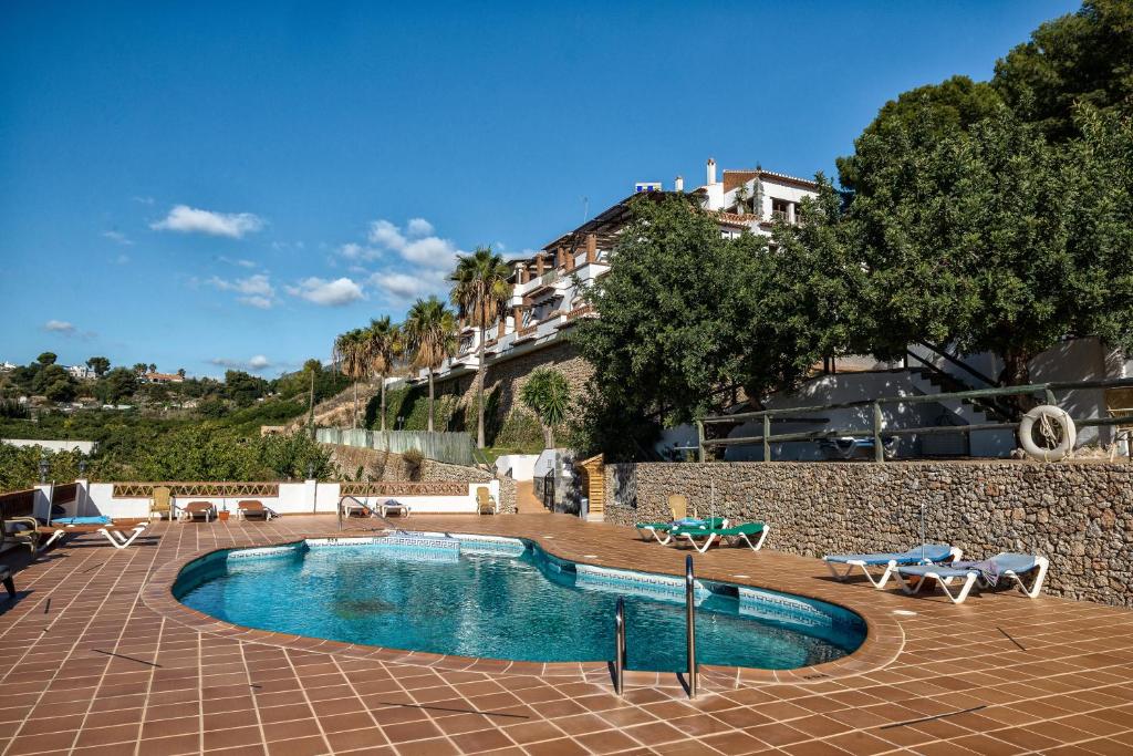 a swimming pool with chairs and a building in the background at Hotel Rural Almazara in Frigiliana