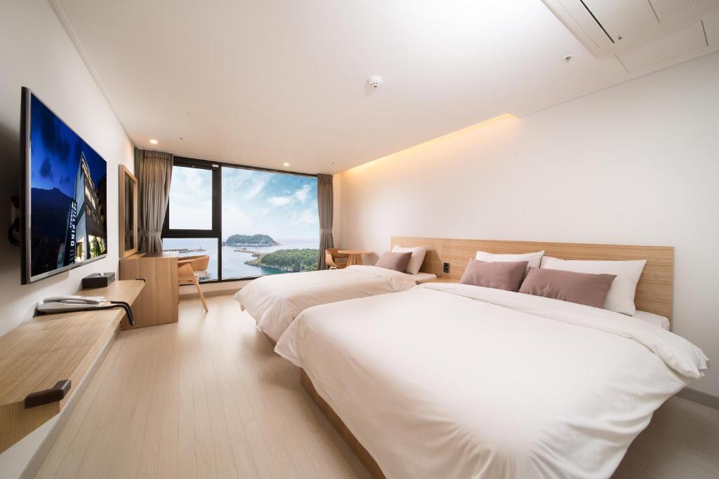a bedroom with two beds and a large window at Pino Hotel in Seogwipo