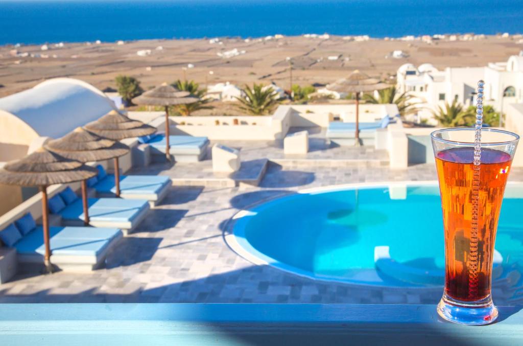 a glass of beer sitting on a table next to a swimming pool at Anemoessa Villa in Oia