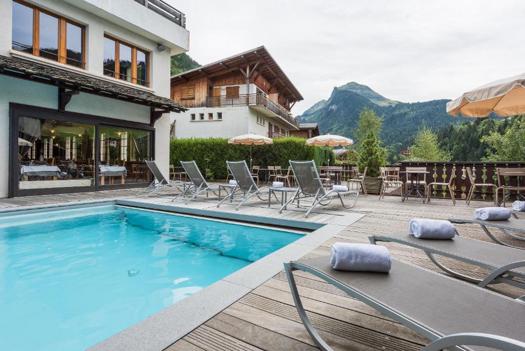 a swimming pool with chairs and tables and a house at Hotel le Petit Dru in Morzine
