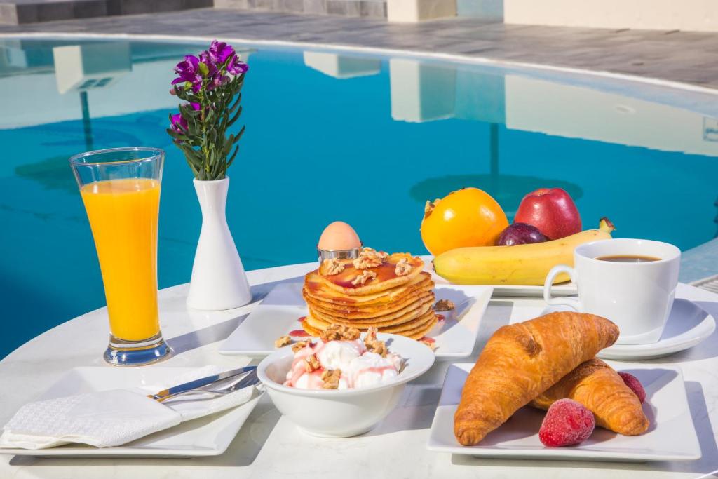 a table with breakfast foods and drinks next to a pool at Anemoessa Villa in Oia