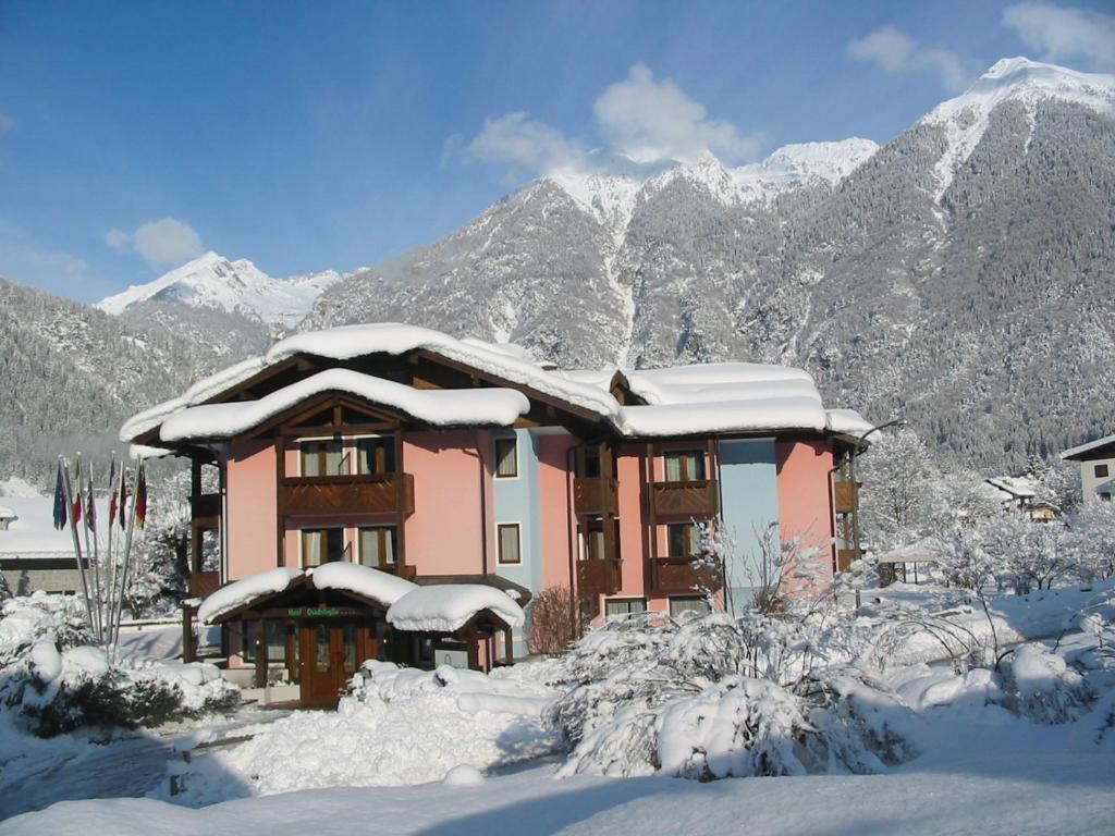 una casa ricoperta di neve con montagne sullo sfondo di Hotel Quadrifoglio a Pinzolo