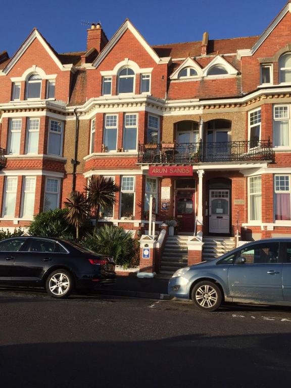 two cars parked in front of a large brick building at Arun Sands Rooms in Littlehampton