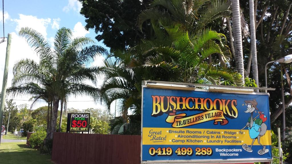 a sign for a building with palm trees in the background at Bushchooks Travellers Village in Bororen