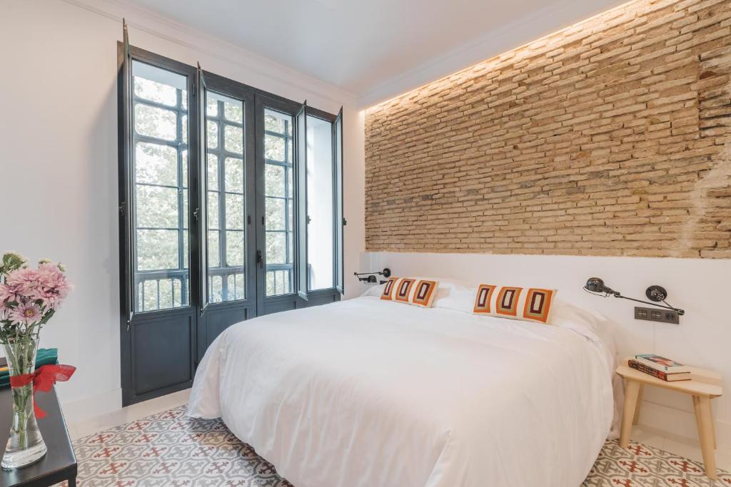 een slaapkamer met een wit bed en een bakstenen muur bij Uma Suites Parada del Marqués in Sevilla
